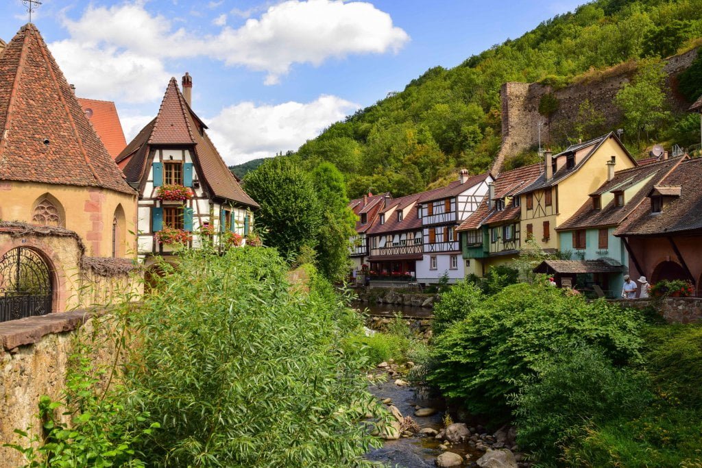 Una foto di Kaysersberg: case tipiche a graticcio, tetti a punta, fiume e vegetazione.